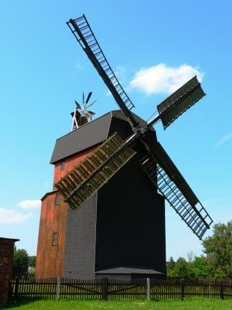 Paltrockwindmühle auf grüner Wiese vor blauem Himmel.