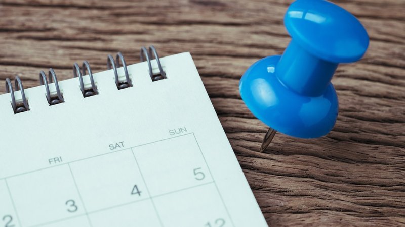 Kalender auf Holztisch mit blauer Pin-Nadel